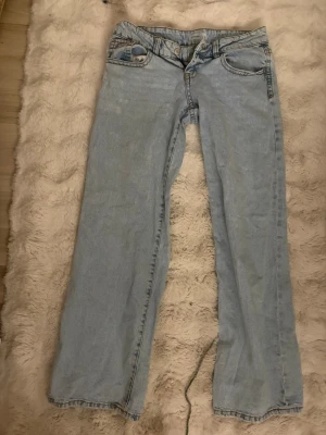 Ljusblå bootcut jeans - Säljer ett par ljusblå bootcut jeans i klassisk denim. Jeansen har fem fickor, bälteshällor och dragkedja med knapp framtill. Perfekta för en avslappnad och trendig look.