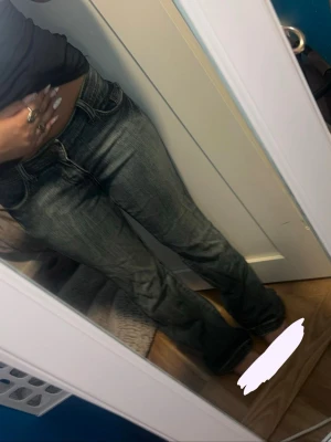 Blå jeans  - Säljer ett par blå bootcut jeans med snygg slitning och unik mönstrad detalj på bakfickan. Jeansen har normal/låg midja och klassisk femficksdesign. Perfekta för dig som gillar en avslappnad men trendig look.