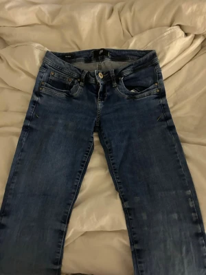 Blå jeans från LTB - Snygga blå jeans från LTB med klassisk femficksdesign och bootcut. Jeansen har en mellanblå tvätt med lätt slitning och detaljerade bakfickor. Perfekta för en avslappnad och trendig look.