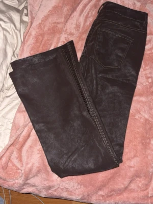 Mörkbruna ”skinn” byxor - Byxor med snygg broderi design längs benen. Aldrig använda. Storlek 38. 