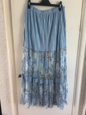 Ljusblå långkjol med blommigt mönster - Långkjol i ljusblått med blommigt mönster och volangdetaljer. Flowy material, perfekt för sommaren! Gott skick, storlek L💗