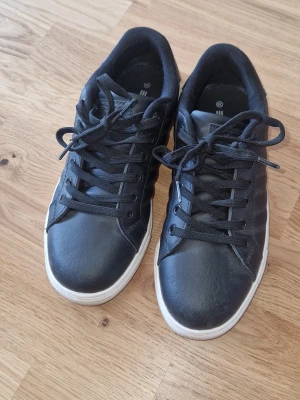 Svarta sneakers - Stilrena svarta sneakers med vit sula och svarta skosnören. Skorna har en klassisk låg modell och är tillverkade i ett slätt material med diskreta sömmar på sidorna. Perfekta för en clean och enkel look. Använda 2 gånger pga att de var för små för mej, de är därför i väldigt finr skick utan defekter el. dyl. 