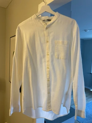 Vit henley-skjorta från Bershka - Vit henley-skjorta från Bershka i bomull med strukturerad yta. Skjortan har lång ärm, bröstficka och knappar framtill. Enkel och stilren design med avslappnad passform och rundad nederkant.