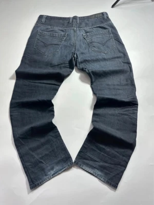 Svarta vintage bootcut jeans - Snygga svarta jeans med bootcut passform och klassiska bakfickor. Jeansen har en rak och något utsvängd benform, perfekt för en avslappnad stil. Tillverkade i denim med tydliga sömmar och detaljer på fickorna. Midja 47cm