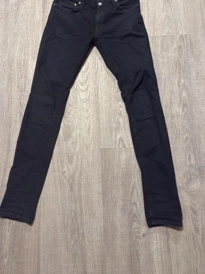 Svarta skinny jeans från nudie - Säljer ett par svarta skinny jeans från  Nudie med klassisk femficksdesign och smal passform. Jeansen har normal midja och är tillverkade i ett stretchigt material som sitter tajt hela vägen ner. Perfekta för en clean och stilren look. 30/32
