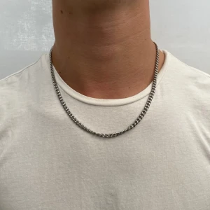 Kedjehalsband Silver - 5mm - Information:  Material: 316L kirurgiskt rostfritt stål  Design: Klassiskt Kedjehalsband Lås: Säker och elegant låsmekanism Längd: 50 cm. Detta kedjehalsband i silver är tillverkat av högkvalitativt 316L rostfritt stål, även känt som kirurgiskt stål. Det är designat för att tåla svett, dusch och bad, vilket gör det perfekt för daglig användning. Halsbandet behåller sin fina silverglans över tid utan att mattas av.🤝