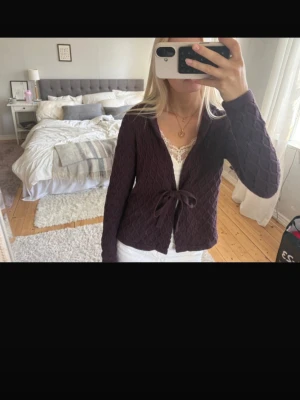 Lila stickad omlott kofta  - Säljer en lila stickad kofta från first class med snyggt diamantmönster och knytband i midjan. Koftan har långa ärmar och en mjuk, mysig känsla. Perfekt att slänga över ett linne eller t-shirt för en chill look.