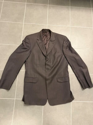 Mörkbrun randig kavaj Ermenegildo Zegna, stl L/42 - Snygg mörkbrun kavaj med diskreta tunna ränder och tre knappar framtill. Klassisk passform med två fickor med lock och en bröstficka. Fodrad insida för extra komfort. Perfekt för en stilren look.