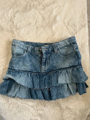 Blå jeanskjol från Gina - Säljer en blå jeanskjol med dubbla volanglager.