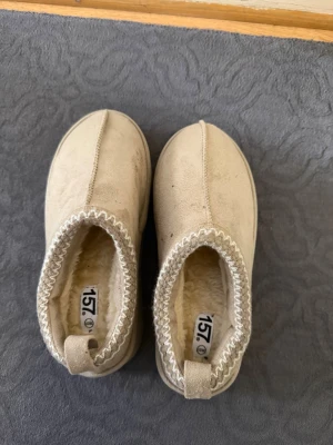 Beige tofflor med ullfoder - Mysiga beige tofflor från 157 med mjukt ullfoder och grov sula. Perfekta för att hålla fötterna varma inomhus. Aldrig använda