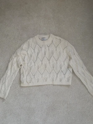 Vit stickad tröja  - Säljer en vit stickad tröja från Only med ett snyggt hålmönster i diamantform. Tröjan har rund halsringning, långa ärmar och ribbade muddar vid ärmslut och nederkant. Jättefint skick.