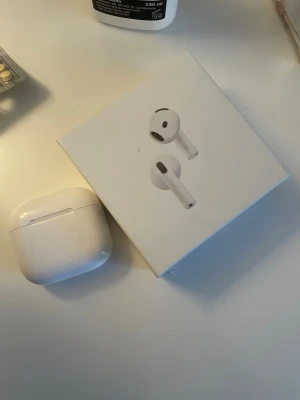 Apple AirPods 4 med laddningsetui - Säljer ett par Apple AirPods 4 med trådlöst laddningsetui. Hörlurarna är vita och har en stilren, kompakt design i plast. Perfekta för musik, samtal och träning tack vare smidig passform och enkel anslutning till iPhone och andra Apple-enheter.