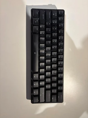 Svart kompakt mekaniskt tangentbord - Säljer ett svart kompakt mekaniskt tangentbord med engelskt QWERTY-layout. Tangenterna har vit text och tangentbordet har en minimalistisk design utan numerisk del. Perfekt för gaming eller skrivande vid datorn. Materialet är plast och det är smidigt att ta med sig. Såklart ingår sladd