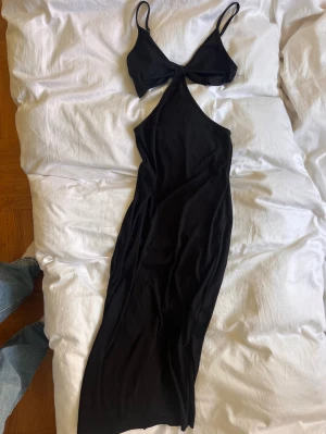 Svart långklänning med cut out - Svart långklänning från SHEIN med smala axelband och cut-out detalj framtill. Klänningen har en tight passform och är tillverkad i ett stretchigt syntetmaterial. Perfekt för dig som vill ha en stilren och trendig look.