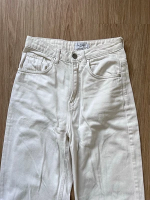 Cremevita raka jeans från NA-KD - Säljer ett par cremevita raka jeans från NA-KD hög midja. Enkel design med knapp och dragkedja, samt trendiga slitsar vid bensluten.