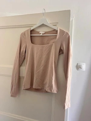 Beige långärmad topp med fyrkantig ringning - Snygg beige långärmad topp med fyrkantig ringning i strl S. Tillverkad i mjukt matierial som känns skön mot huden och sitter som en smäck. Perfekt att styla med jeans eller kjol för en clean look.