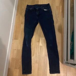 Nudie Jeans  - Säljer ett par feta mörkblå jeans från Nudie jeans med klassisk femficksdesign och smal passform. Jeansen har en diskret tvättad look och Nudie -logga på bakfickan. 