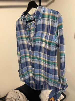 Blågrön rutig skjorta från Ralph Lauren - Säljer en klassisk rutig skjorta från Ralph Lauren i blå, grön och vit färg. Skjortan har knappar framtill, lång ärm och button-down krage. Tillverkad i mjuk bomull som känns skön mot huden. Perfekt för en avslappnad men ändå stilren look. Skjortan är i storlek xs men passar upp mot M. Modellen är 182cm 73kg.