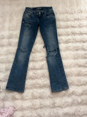 Blå bootcut jeans från LTB - Säljer ett par blå bootcut jeans från LTB, modell Valerie. Jeansen har slitna detaljer och hål på låret och knät för en trendig look. Klassisk femficksmodell med dragkedja och knapp. Perfekta för dig som gillar en avslappnad men snygg stil.