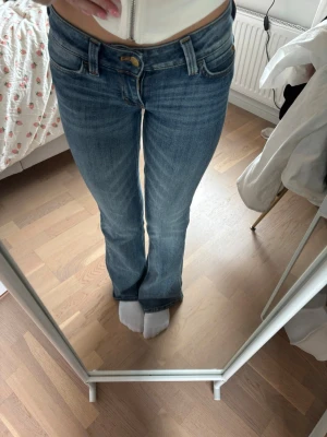 Blå bootcut jeans med slitningar - Säljer ett par blå bootcut jeans med lätt slitna detaljer och klassisk femficksmodell. Jeansen har en snygg tvätt och markerade sömmar. Perfekta för dig som gillar en avslappnad men trendig stil.
