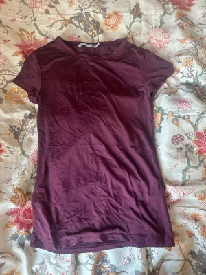 Vinröd t-shirt från 157 - En enkel och stilren vinröd t-shirt från 157 i storlek M. T-shirten har rund halsringning och korta ärmar. Tillverkad i mjuk bomull som känns skön mot huden. Perfekt basplagg att matcha med jeans eller kjol. Passar S