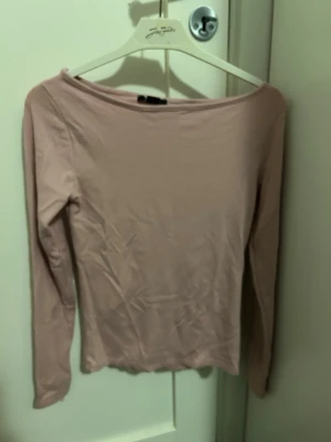Ljusrosa långärmad topp från NewYorker - Säljer en enkel och stilren ljusrosa långärmad topp från NewYorker. Toppen har en bred, båtringad hals och är figurnära i modellen. Perfekt att matcha med jeans eller kjol för en clean look. Tröjan är i storlek M.