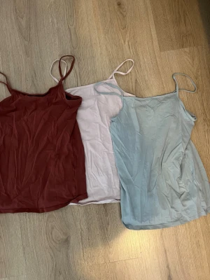 3-pack linnetoppar från H&M - Säljer tre stilrena linnetoppar från H&M i färgerna rostbrun, ljusrosa och ljusblå. Alla har tunna axelband och en enkel, rak passform. Perfekta att matcha till olika outfits och superbekväma under varma dagar.