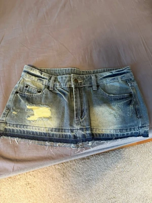 Blå jeans minikjol  - Säljer en kort blå jeanskjol med slitna detaljer. Har aldrig använt. Skriv om ni undrar något ! 