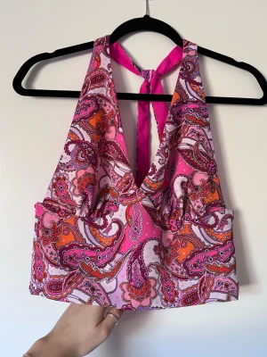 Halterneck topp med mönster (NY) - Mönstrad halterneck topp med knytning i nacken. Toppen går att vända ut och in beroende på om man vill h den mönstrad eller helt rosa. Resår på baksidan för en perfekt passform mot kroppen! Aldrig använd 🩷