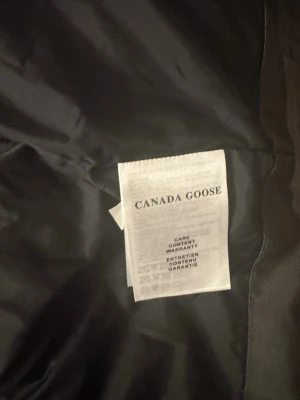 Svart dunjacka från Canada Goose - Säljer en svart dunjacka från Canada Goose med klassisk design. Jackan har en slät yta, diskret innerfoder och detaljer som meshficka på insidan. Perfekt för kalla vinterdagar tack vare det varma dunfodret och den tåliga ytterytan. har också Canada goose påse