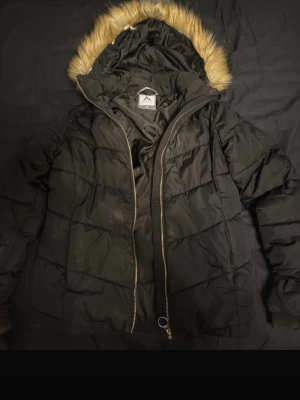 Svart pufferjacka med fuskpäls - Säljer en svart pufferjacka från mckinley med huva och beige fuskpäls. Jackan har dragkedja framtill, två sidofickor och quiltad design. Perfekt för kalla vinterdagar och riktigt mysig att bära.