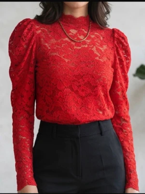 Röd spetsblus med puffärm - Trendig röd blus i spets med höghalsad krage och puffiga långärmar. Blusen har ett genombrutet spetsmönster och figurnära passform, perfekt för att sticka ut. Materialet är lätt och luftigt, vilket ger en elegant look.