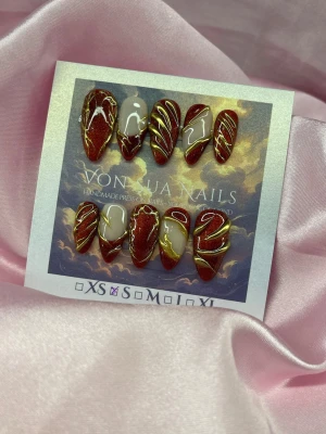 RubyLuxe (S);Medium Almond - Handgjorda press-on naglar i vinrött med skimrande röd cateye finish, dekorerade med handmålde tunna guldfärgade linjer och inslag av nude och vitt. Medium längd och mandelformade, och riktigt trendiga, perfekta för dig som vill ha något unikt och snyggt. S: 15 mm, 11,5 mm, 12 mm, 11 mm, 9 mm 