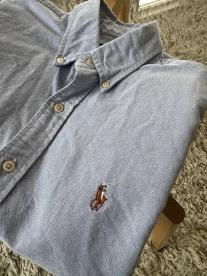 Ralph Lauren Skjorta Ljusblå - Ralph Lauren skjorta i 100% bomull. Sommrig ljusblå färg. Jättefint skick, inga skavanker. Mått:  •Axel-Axel: 44cm •Axel-Midja: 61cm •Armhåla-Armhåla: 49cm  Hör av dig vid frågor eller funderingar! Postas senast 24 timmar efter frakt!🫶  #ralphlauren #shirt #skjorta #sommar #svergievinted #finland #vinted #svergie