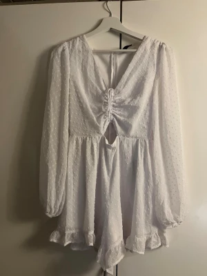 Vit kort klänning med snörning - Söt vit kortklänning med prickigt strukturmönster, v-ringning och snörningsdetalj framtill. Klänningen har långa, puffiga ärmar. Den har shorts, men på så ser det ut som en klänning. Köpt för några år sedan, men knappt använd🩷                                    Den har en reva på sidan, i resåren  men det går lätt att sy ihop.💕🌟