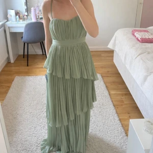 Grön balklänning  - Ljusgrön långklänning med volanger från märket Lulus. Aldrig använd med prislapp kvar. Jag är 162 cm lång, har på mig 8 cm klackar på bilderna och då är klänningen lite för lång för mig. 