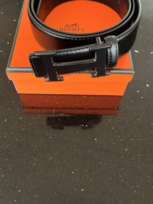 Svart skärp från Hm med Hm-spänne - Snyggt svart skärp från hm med det ikoniska Hm spännet i svart metall. Bältet är gjort i exklusivt skinn och levereras i original orange Hm -box. Perfekt accessoar för att lyfta din outfit.