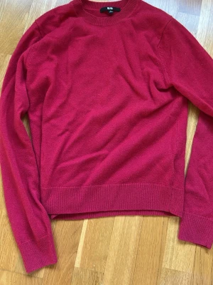 Röd stickad tröja från Uniqlo - Snygg röd stickad tröja från Uniqlo med rund halsringning och långa ärmar. Tröjan har ribbade muddar vid ärmslut och nederkant, vilket ger en klassisk och stilren look. Perfekt att matcha med jeans eller kjol.