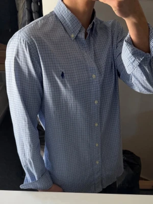 Blårutig skjorta från Ralph Lauren - Klassisk blårutig skjorta från Ralph Lauren med button-down krage och lång ärm. Skjortan har små vita och blå rutor, broderad logga på bröstet och knappar framtill. Perfekt till jeans eller chinos för en clean och stilren look. Nypris ca 1400kr🙌🏼