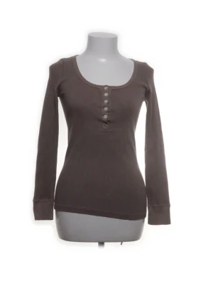 Brun långärmad ribbad topp - Snygg brun långärmad topp med ribbad struktur och rund halsringning. Toppen har knappdetaljer framtill och är figurnära i modellen. Perfekt att styla med jeans eller kjol för en avslappnad look.