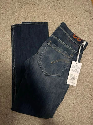 Dondup George - 2800kr Nya med tags. Säljer ett par mörkblå jeans från Nudie Jeans med slitningar och hål på vänster lår. Klassisk femficksmodell med kontrastsömmar och smal passform. Jeansen har en snygg tvättad look och är tillverkade i bomull. Perfekta för en avslappnad stil.