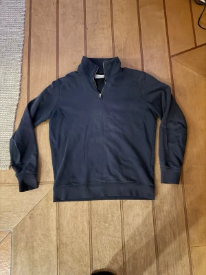 Mörkblå half-zip tröja These Glory Days - Mörkblå sweatshirt med half-zip från These Glory Days. Tröjan har hög krage, långa ärmar och ribbade muddar. Tillverkad i mjukt bomullsmaterial som känns skönt mot huden. Perfekt för en avslappnad och stilren look.