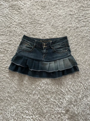 Blå volangkjol Lågmidjad  - En Lågmidjad jeanskjol omsydd från ett par jeans.  Stretchig   Midjemått tvärsöver: 37cm Längd: 32cm