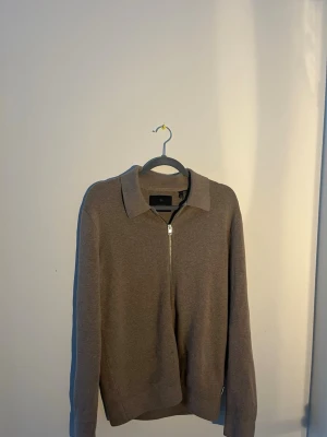 Beige kofta med dragkedja Jack & Jones - Snygg beige kofta från Jack & Jones med klassisk krage och hel dragkedja framtill. Stickad i mjukt material som passar perfekt till lager-på-lager. Långärmad och stilren design som funkar till många olika looks.