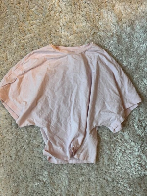 Ljusrosa oversized t-shirt från Nelly - Säljer en ljusrosa oversized t-shirt från Nelly. T-shirten har korta, vida ärmar och är gjord i mjuk bomull. Perfekt för en avslappnad och chill stil. Enkel design utan mönster eller detaljer.