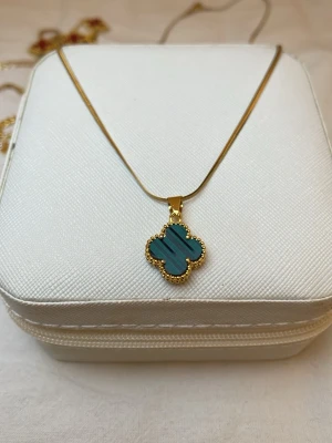Guldhalsband  - Snyggt halsband i guld med ett hänge i form av en fyrklöver. Hänget har en turkos sten och är dekorerat med små guldfärgade pärldetaljer runt kanten. Perfekt accessoar för att lyfta din stil.