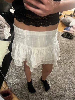 Vit volangkjol i bomull - Supersöt vit kortkjol med volanger och lätt struktur i tyget. Kjolen har en bred midja och är gjord i ett tunt, luftigt bomullsmaterial. Perfekt för varma dagar och enkel att styla med olika toppar. Inbyggda shorts