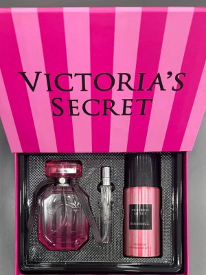 Victoria's Secret Bombshell presentset - Lyxigt presentset från Victoria's Secret med parfym, miniflaska och deodorant i doften Bombshell. Förpackningen är rosa med ränder och svart inredning. Flaskan är elegant och genomskinlig med rosa detaljer och svart band.