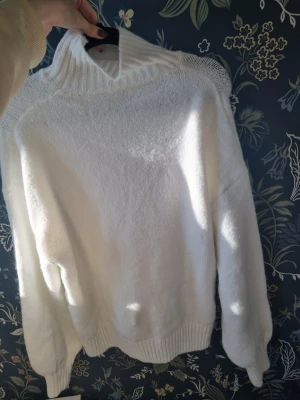 Vit stickad polotröja - Klassisk vit stickad polotröja med ribbad hög krage och muddar vid ärmslut och nederkant. Tröjan har en avslappnad passform och är perfekt för lager-på-lager. Materialet ser mjukt och mysigt ut, perfekt för kyliga dagar.