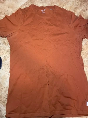 Brun t-shirt från Jack & Jones - Säljer en enkel brun t-shirt från Jack & Jones Essentials i ekologisk bomull. T-shirten har rund halsringning och korta ärmar, perfekt för en avslappnad stil. Passformen är normal och materialet känns mjukt mot huden.